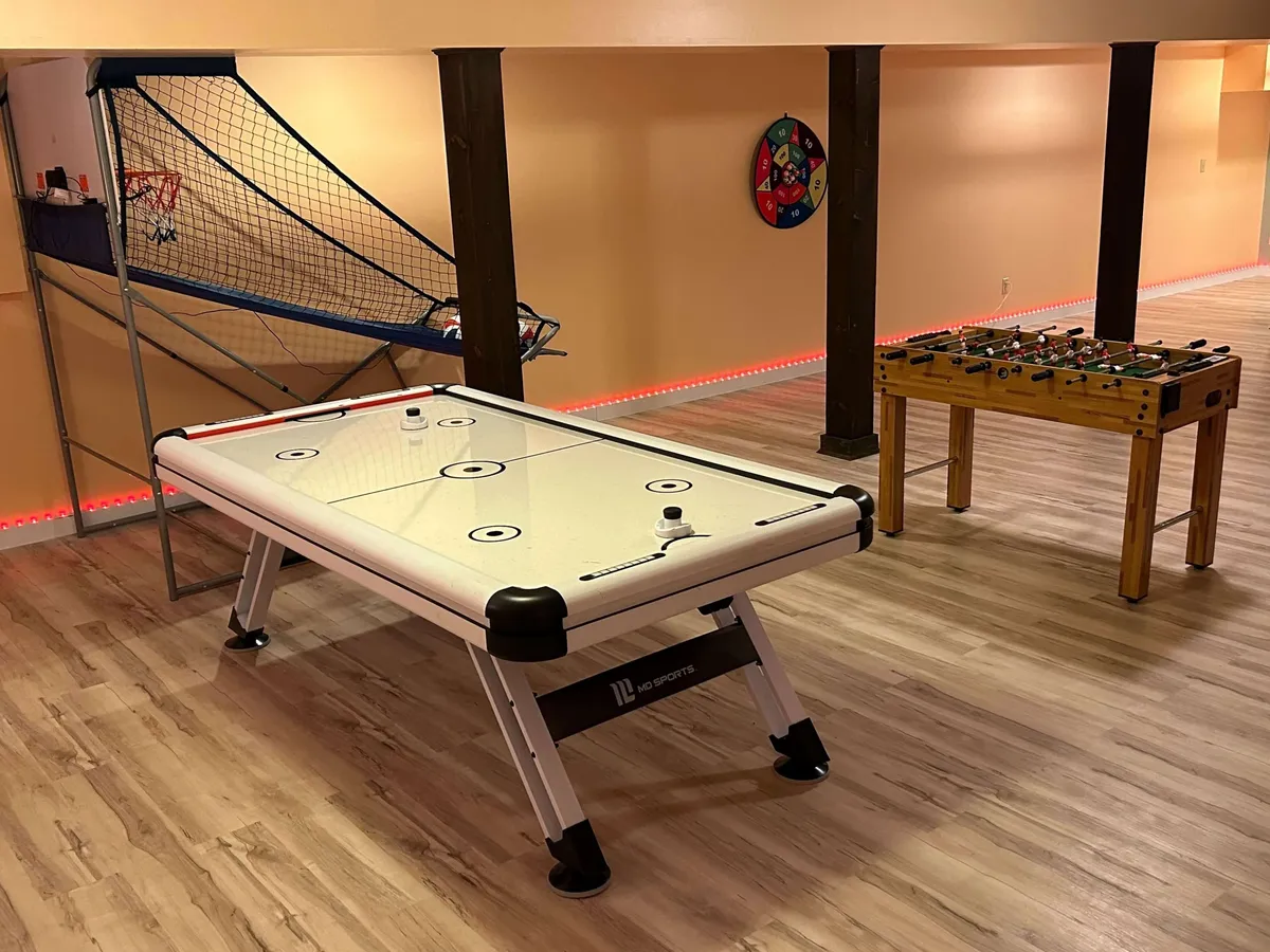 This energetic interior photo showcases a vibrant game room, featuring an air hockey table, foosball table, and a basketball arcade game setup. The room is styled for fun and friendly competition, with ample space for gathering and playing.