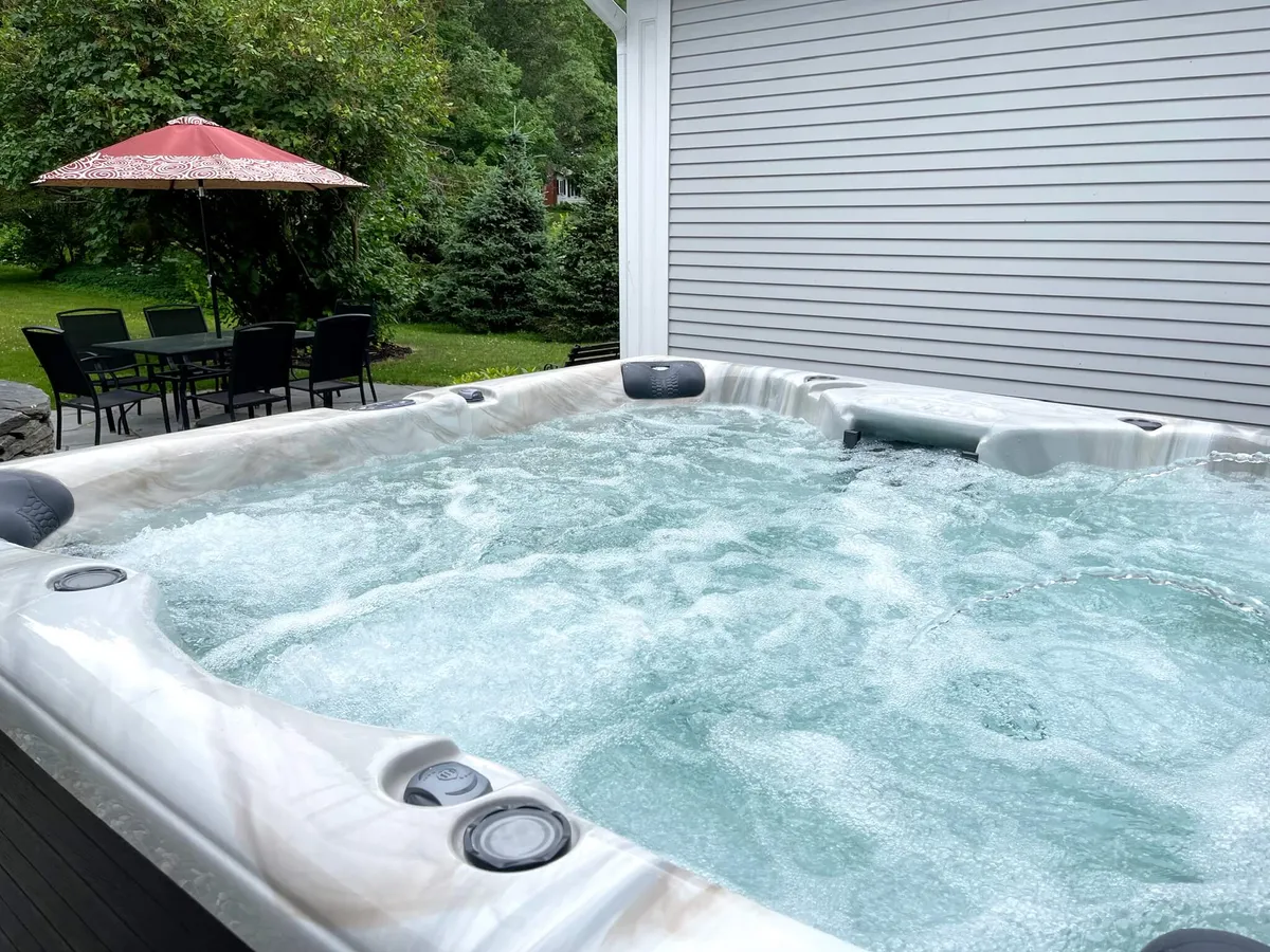 This image features a hot tub, patio table, umbrella, and lush greenery. The scene invites relaxation and social gatherings, suggesting a fun spot for families to reconnect under the stars after busy days.