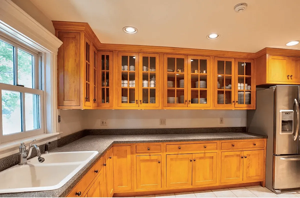 A warm, inviting kitchen featuring rich wooden cabinets, a sleek stainless steel refrigerator, a spacious granite countertop perfect for meal preparation, and a sunlit window. The scene captures the heart of the home during a lively family gathering or festive culinary experiment.