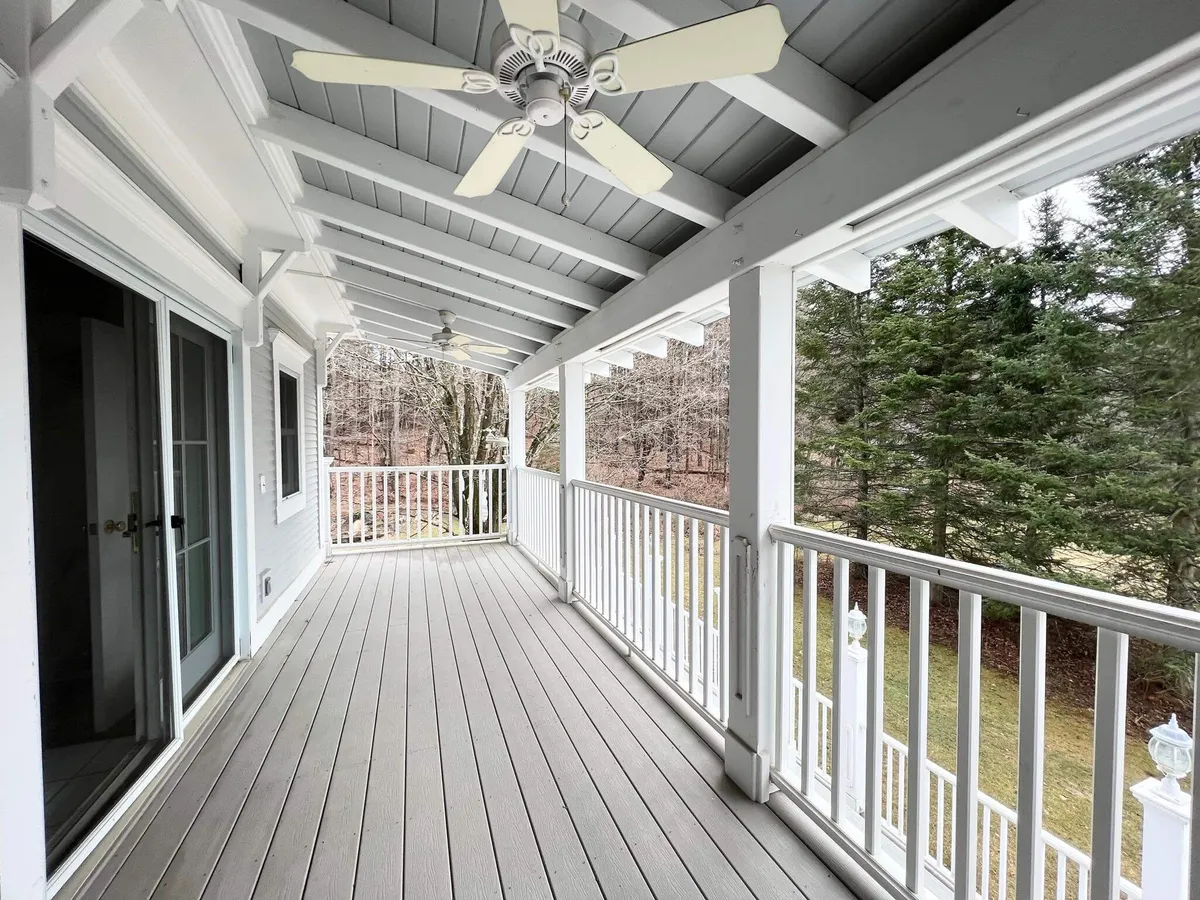This exterior image features a classic porch with a ceiling fan, sturdy wooden flooring, and is surrounded by lush trees. The setting suggests a tranquil place for relaxing, reading, or enjoying nature, with ample space for a group to gather in the fresh air.