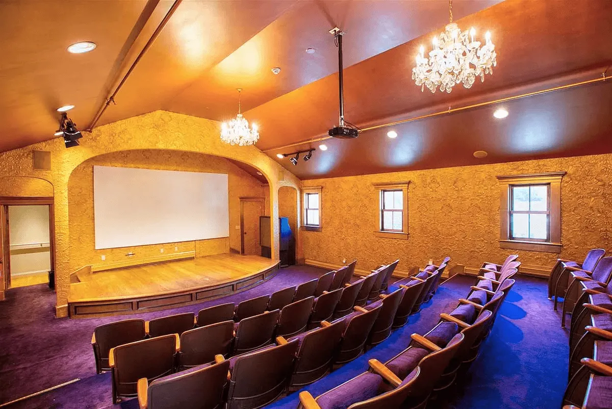An elegant, theater-style room with a stage, large screen, chandeliers, and plush audience seating. The space is inviting and sophisticated, designed for immersive film screenings and memorable movie nights.
