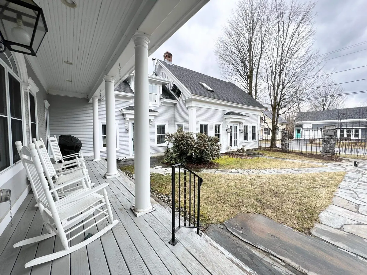 A welcoming porch with classic rocking chairs overlooks a well-maintained stone pathway and lush landscape, suggesting a peaceful spot for group conversations or unwinding after a day of learning or adventure.